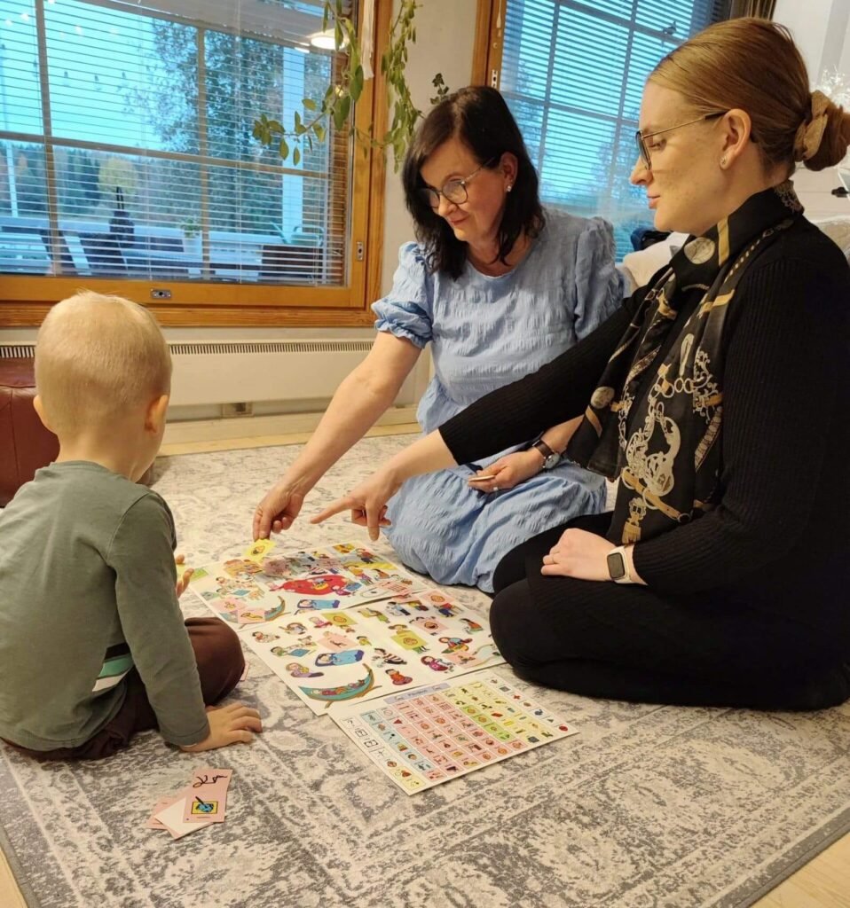 Tulkki Virpi, asiakas ja lapsi tutkivat Kipinäkeskuksen materiaalia kommunikaatio-opetuksen ja -ohjauksen yhteydessä.